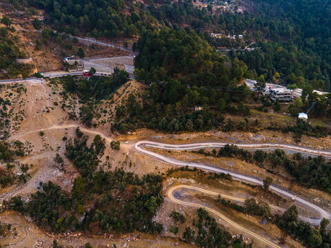 Aerial view of winding mountain roads with sharp hairpin turns traversing a lush green hillside near Dino Valley in Islamabad, Islamabad Capital Ter, Pakistan.