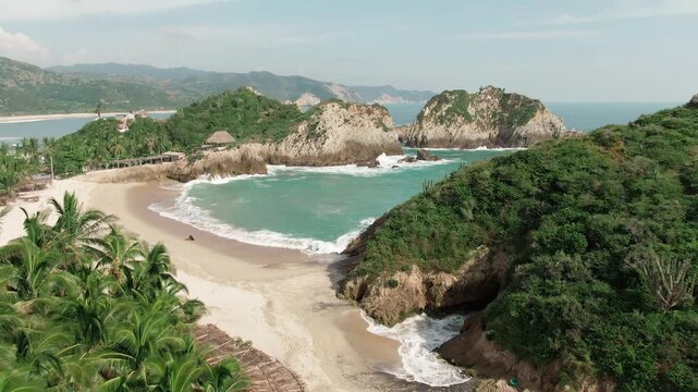Maruata Viejo and Maruata beach with white sand and tropical vegetation on the Pacific coast. Dolly in aerial toward Dedo de Dios landmark