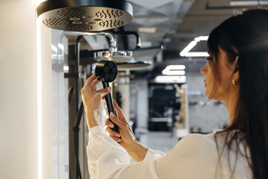 Female bathroom designer inspects modern showerhead in a contemporary showroom with various fixtures and lighting elements visible in the background