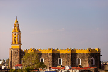 Obraz premium Exterior view of the Royal Chapel of Naturales in Cholula, featuring its distinctive yellow facade with crenellations and stone bell tower against a clear sky