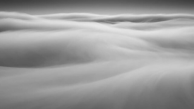 Slow tracking aerial motion of low cloud layers flowing and rolling over horizon in monochrome sky above open atmosphere at dawn