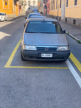Fiat Tempra sedan parked on an Italian city street with yellow parking lines, urban architecture background