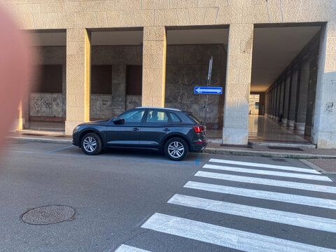 Audi Q5 dark grey SUV parking on urban street next to zebra crossing and classic architecture building during daytime