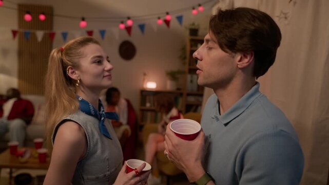 Side view waist up shot of Caucasian young adult woman and man talking and drinking from red cups at Independence Day party. Clip is perfect for holiday marketing and youth lifestyle commercials