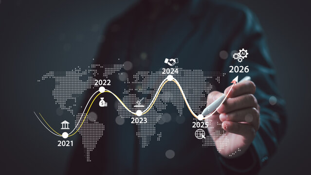 Unrecognizable businessman holding stylus pen draws rising growth line chart showing global financial progress starting 2021 until 2026 over world map background inside dark office studio setting now.