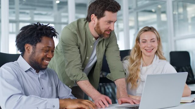 Diversity three businesspeople business team looking in laptop monitor talking smiling cooperation. Caucasian businessman CEO talk to multiracial workers explain computer work smile laugh in office