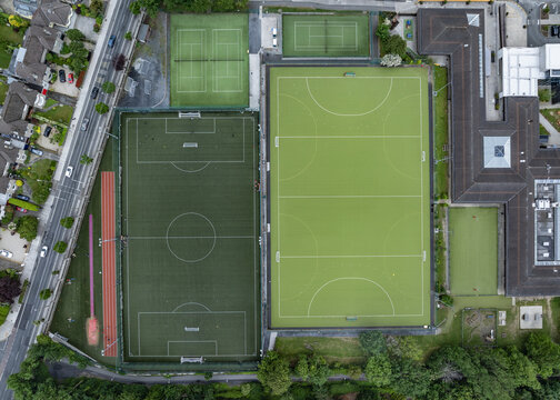 Aerial view of St. Kilian's German School sports fields featuring a football pitch and hockey field with green artificial turf and buildings in Dublin, County Dublin, Ireland.