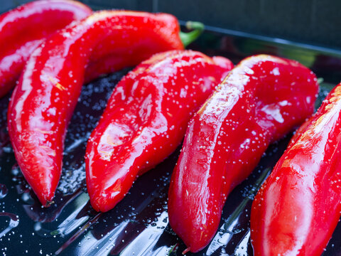 Fresh Red Romano Peppers on a Gas Grill. Close-up of salted and oiled red romano peppers on a black sheet on a gas grill being grilled for a vegetarian meal.