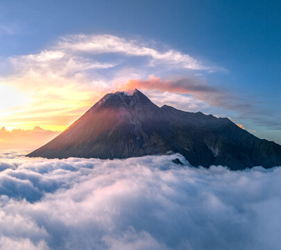 Aerial view of Mount Merapi volcano peak rising above a thick sea of clouds during a golden sunrise in Cangkringan, Daerah Istimewa Yogya, Indonesia.