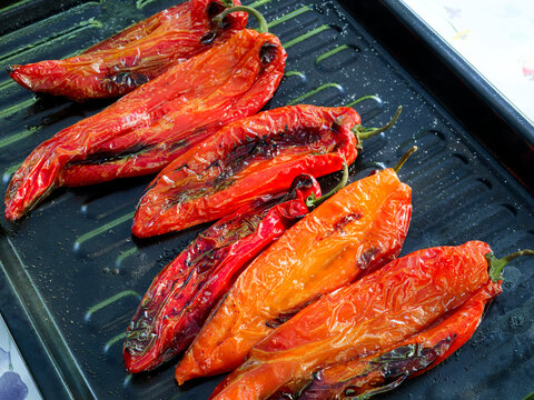 Salted and oiled red romano peppers ready grilled on a black sheet on a gas grill being grilled for a vegetarian meal. 