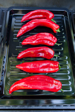 A high-angle close-up shot of a modern gas grill filled with salted and oiled red romano peppers on a black sheet on a gas grill being grilled for a vegetarian meal.