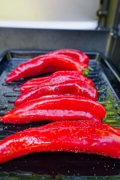 A high-angle close-up shot of a modern gas grill filled with salted and oiled red romano peppers on a black sheet on a gas grill being grilled for a vegetarian meal.