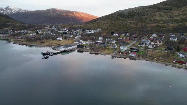 Aerial drone sideways tracking shot over still lake reflecting sunset glow with town, Troms&oslash;, Norway