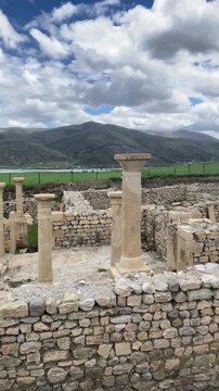 Ancient ruins of Satala Ancient City in Kelkit, G&uuml;m&uuml;şhane, T&uuml;rkiye. Historic Roman archaeological site featuring stone foundations and columns set against a dramatic cloudy sky and lush green landscap