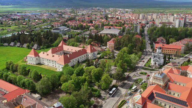 Aerial drone view of a white castle with red roof and towers above a town and hills, Harghita, Transylvania, Romania.