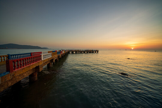 Sun rising over the East Sea beside a colorful pier, creating a peaceful coastal morning scene.