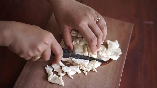 Close up woman hand slicing beef fat (suet) on wooden cutting board for tallow making, traditional food preparation process