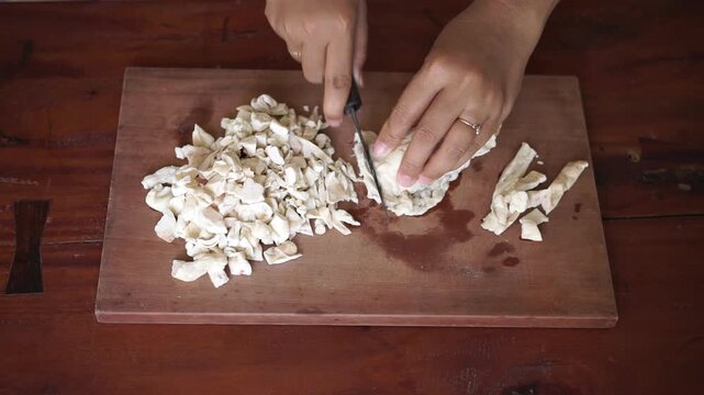 Overhead view of woman hand cutting beef fat (suet) into small cubes on wooden cutting board, food preparation for tallow making