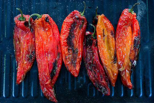 Salted and oiled red romano peppers ready grilled on a black sheet on a gas grill being grilled for a vegetarian meal. The scene captures healthy, vegan outdoor cooking during a bright summer day.
