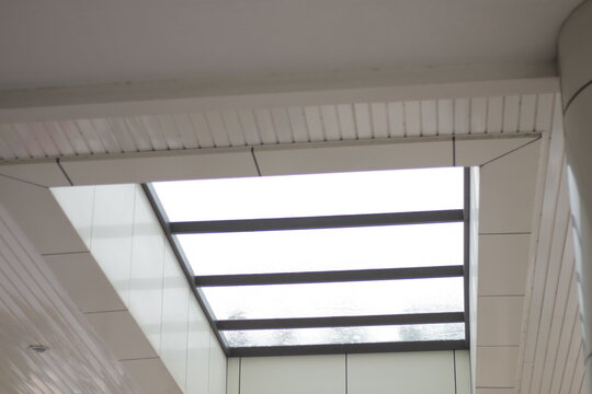 Modern glass skylight canopy on a white minimalist building ceiling with metal frame structures.
