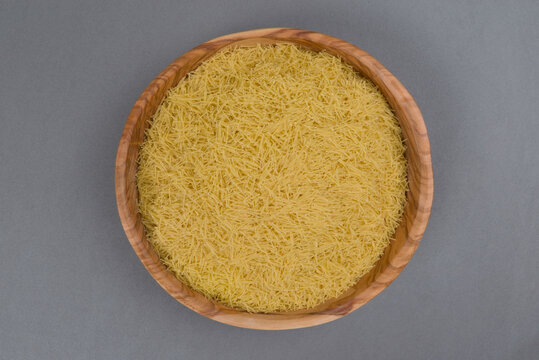 Cuenco de madera lleno de fideo capellini sobre fondo gris