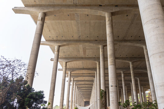 Low-angle perspective view of massive concrete pillars supporting a large bridge or runway extension. The industrial structure features numerous tall columns and a gray deck.