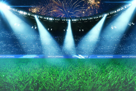 Empty green soccer field of a huge stadium with bright spotlights, fans in the stands and spectacular fireworks in the night sky during a match opening ceremony. Professional sport arena background.