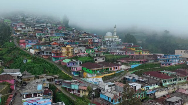 Aerial view of Nepal Van Java colorful houses on a misty hillside with a mosque and lush greenery in Kecamatan Kaliangkrik, Jawa Tengah, Indonesia.