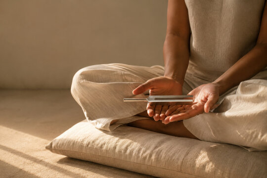Person practices tuning fork therapy while sitting in serene environment, promoting relaxation and mindfulness