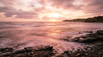 Obraz premium The sun rises over a rocky coastline, casting a warm glow on the ocean and sky. Waves gently crash against the dark, textured rocks.
