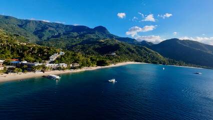 Obraz premium Tropical resort coastline in Asia. Aerial view of a popular beach destination with turquoise waters, white sand and lush mountains.