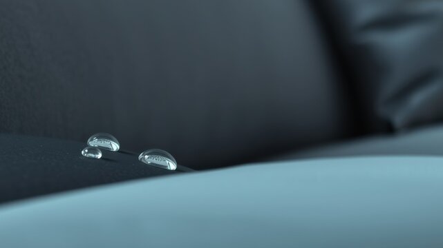 Close-up of water droplets on a dark-colored, water-resistant surface demonstrating excellent liquid repellency