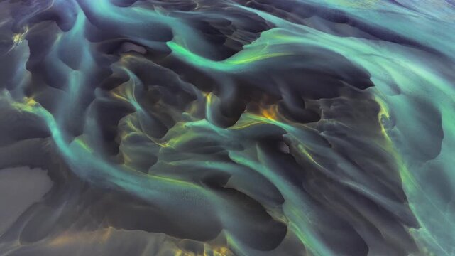 Aerial view of abstract glacial river patterns with swirling turquoise water and dark volcanic sediment in Hella, Rangarthing ytra, Iceland.