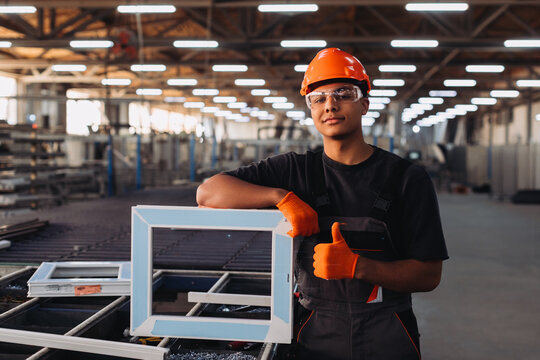 Young worker making thumbs up sign in window factory