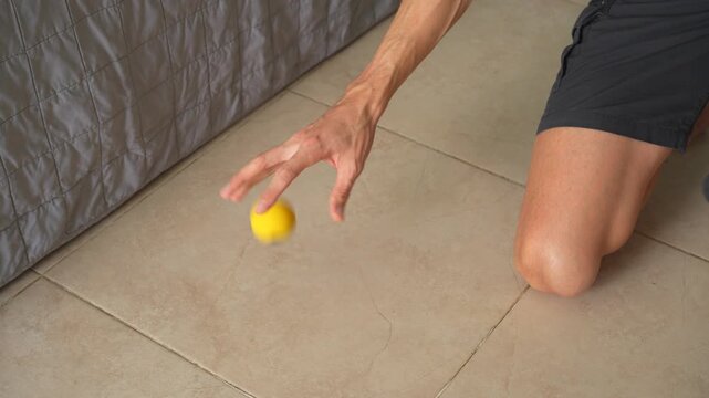 Man bouncing very small yellow rubber ball on the floor in close up with high quality sound. Sensory movement, focus and tactile interaction concept.