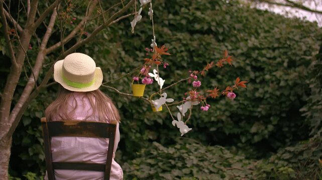 Woman wearing Easter bonnet and sits by easter decorations on blossom tree