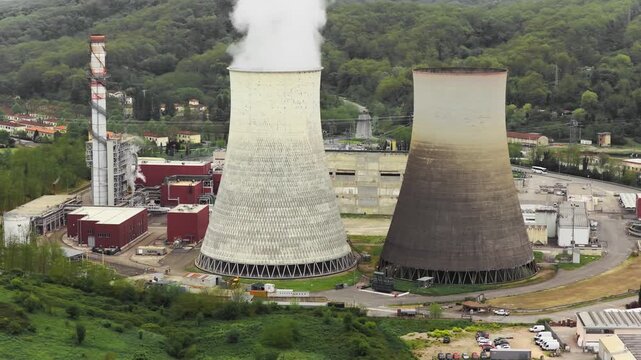 Aerial view of the Centrale Termoelettrica Santa Barbara Enel power plant with cooling towers and steam surrounded by green hills in Santa Barbara, Toscana, Italy.