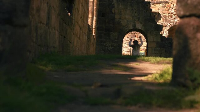 Woman jumping in Kirkstall Abbey Church ruins arch windows in Leeds Yorkshire