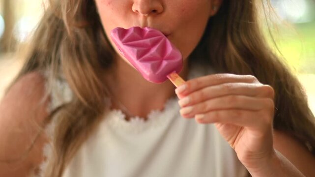 Woman enjoying refreshing pink ice cream pop on summer day.