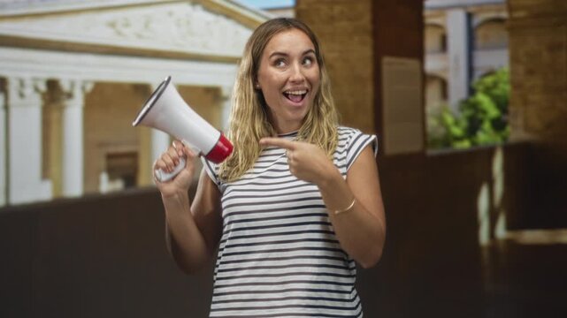 Woman holding megaphone points finger to megaphone in museum hall while smiling and facing camera; cheerful announcement.