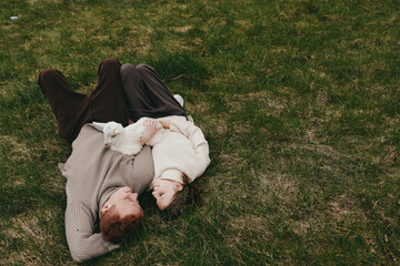 Lifestyle shot of a couple lying on grass embracing softly, with a playful goat kid nearby, capturing warm affection and natural connection in an outdoor rural setting. © SHOTPRIME STUDIO