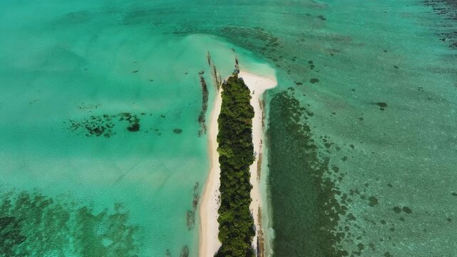 Aerial view of a narrow tropical island with lush green vegetation and white sand beaches surrounded by turquoise water and coral reefs in Fulhadhoo, Baa Atoll, Maldives.