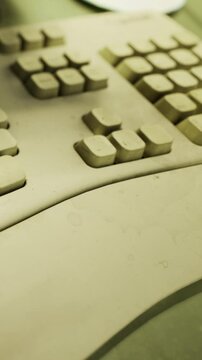 A close up view of a dirty computer keyboard with missing key labels. The keyboard rests on a desk with a faint green background. Dust and wear are visible on several keys.