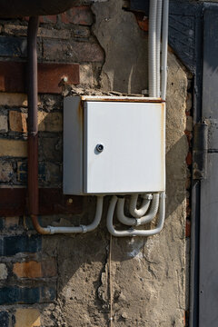 A Rusty Electrical Junction Box Mounted on a Brick Wall Surrounded by Exposed Wiring, Highlighting Urban Infrastructure and Its Aesthetic Decay