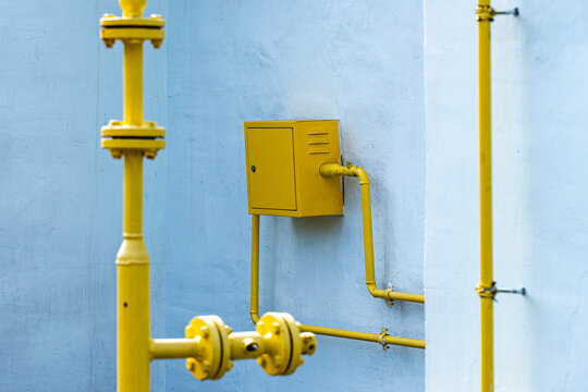 A striking contrast of yellow pipes and a utility box against a soft blue wall, showcasing industrial design elements and vibrant color interplay in urban settings