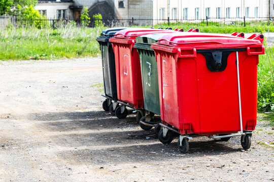 Colorful Trash Bins Lined Up Along a Gravel Path with Lush Green Grass and Urban Background in Bright Daylight