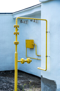 Detailed View of Industrial Yellow Pipes and Fittings Attached to a White Exterior Wall, Highlighting Structural and Functional Aspects of Plumbing Systems