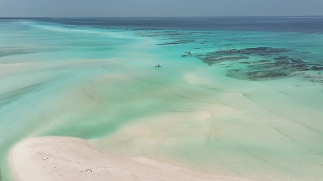 Aerial view of pristine white sandbars and crystal clear turquoise waters with a small boat and coral reefs in Fulhadhoo, Baa Atoll, Maldives.