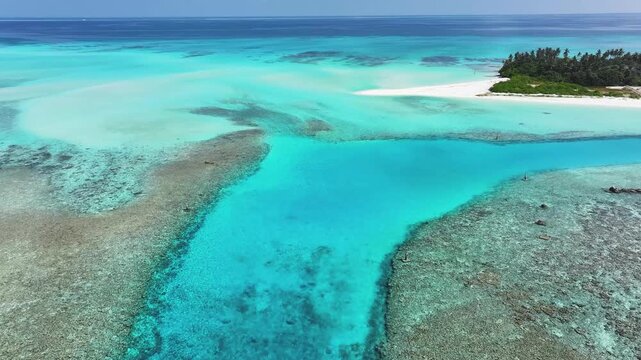 Aerial view of crystal clear turquoise waters, vibrant coral reefs, and a white sand beach with palm trees on the island of Fulhadhoo, Baa Atoll, Maldives.