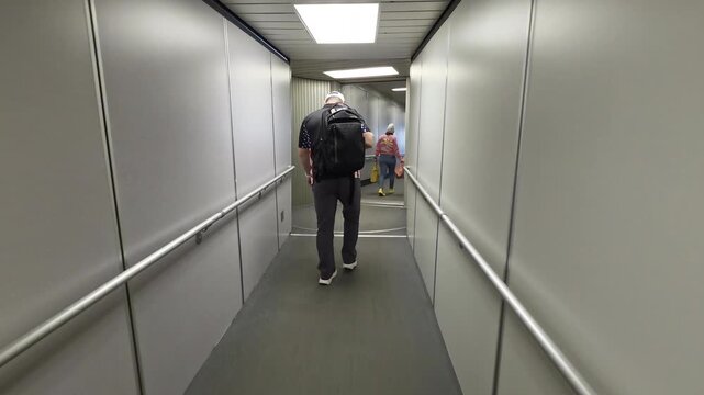 Passengers Walking Through Narrow Airport Jet Bridge Corridor, Travel video frame showing boarding walkway, gray walls and people moving to plane